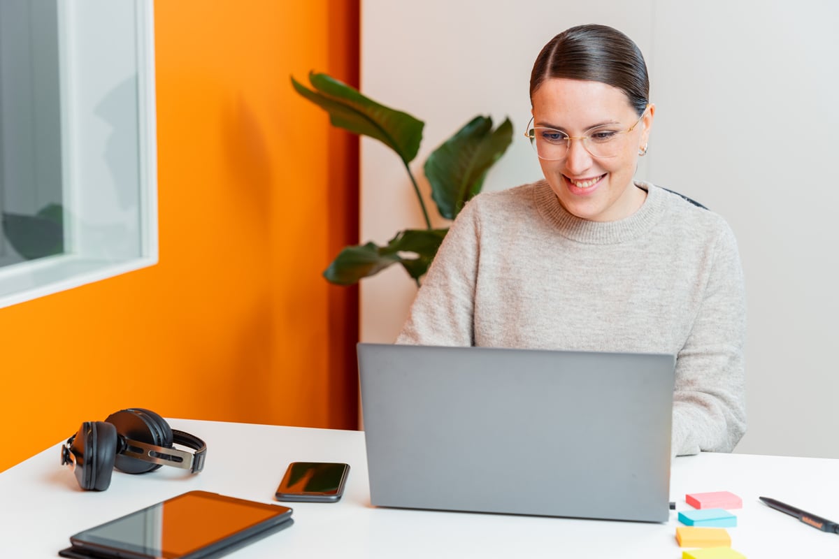 Kvinna sitter leende framför ett skrivbord och arbtar på en dator