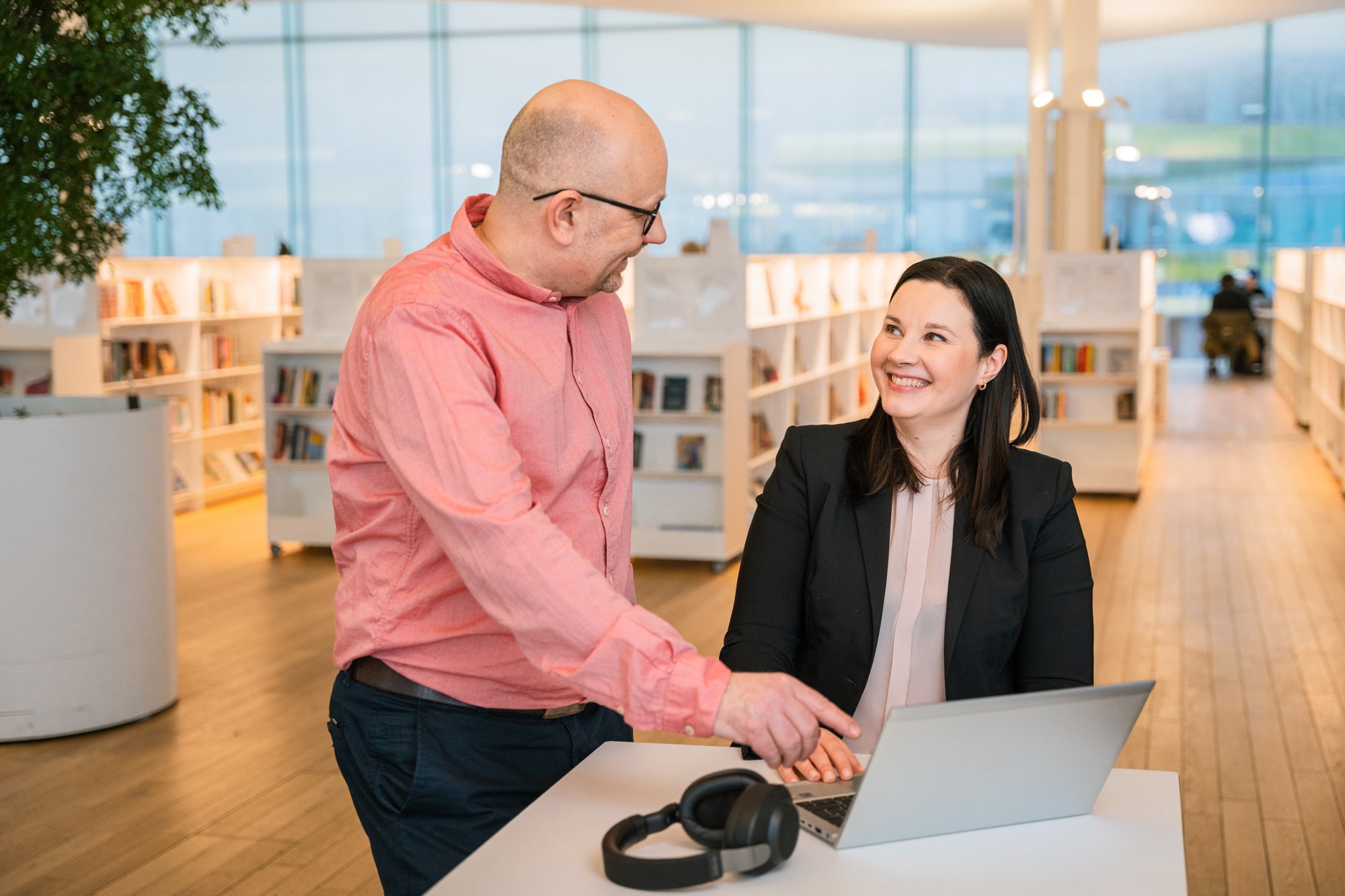 Föreläsare visar leende kvinna onlinekurser på en dator i ett bibliotek
