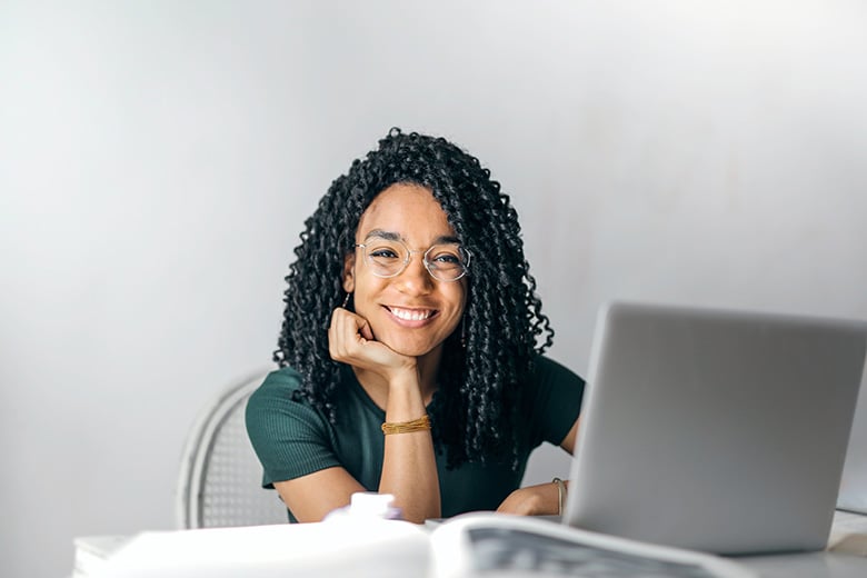 Kvinna sitter framför en dator och tittar leende mot kameran