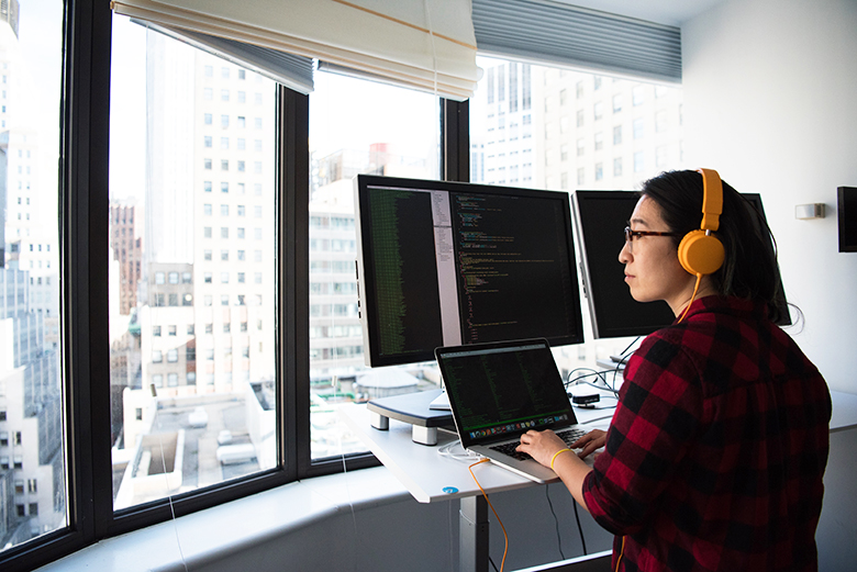 Kvinna arbetar framför flera datorskärmar och tittar ut på ett kontorslandskap